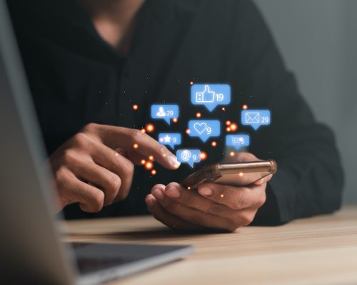 Man using a social media marketing concept on mobile phone with notification icons of like, message, comment and star above smartphone screen.