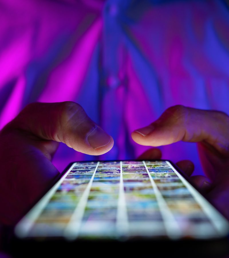 man scrolling mobile phone screen in dark room with neon lights. internet browsing, social media and marketing
