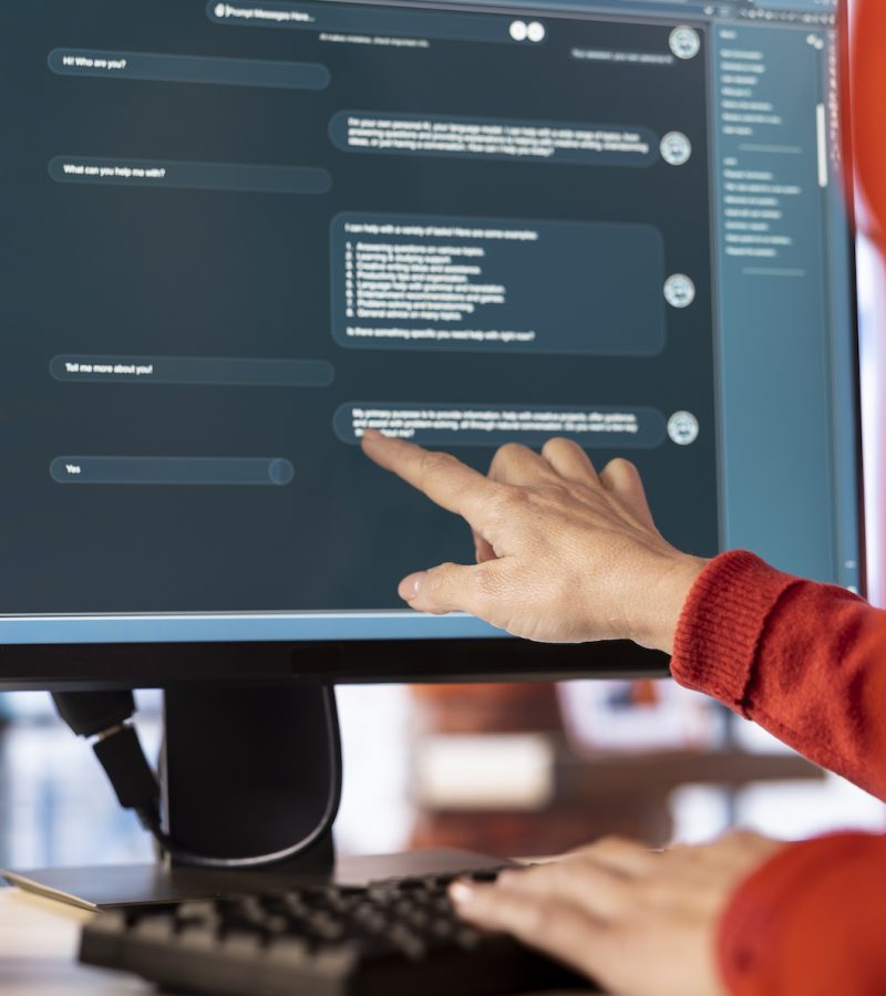 Woman uses AI chatbot system on a computer to guide her through problem solving tasks, futuristic technology highlights smart algorithms and machine learning. Online communication and support.