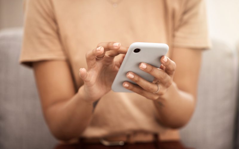 Hands, phone and woman typing on sofa in home living room, texting or scrolling social media. Tech, relax and female on couch in lounge on mobile smartphone networking or internet browsing in house